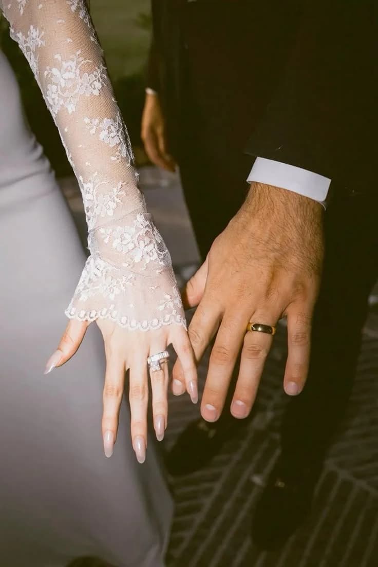 A bride and groom's hands rest together, a slim ring on each finger.