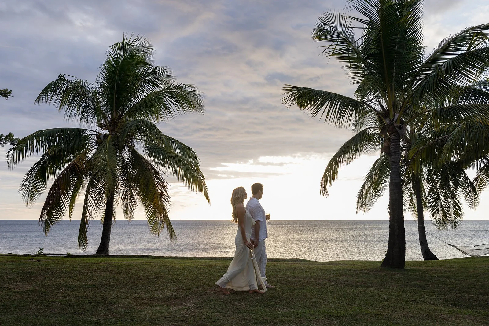 A couple walks together on a tropical beach at sunset, framed by coconut palms.